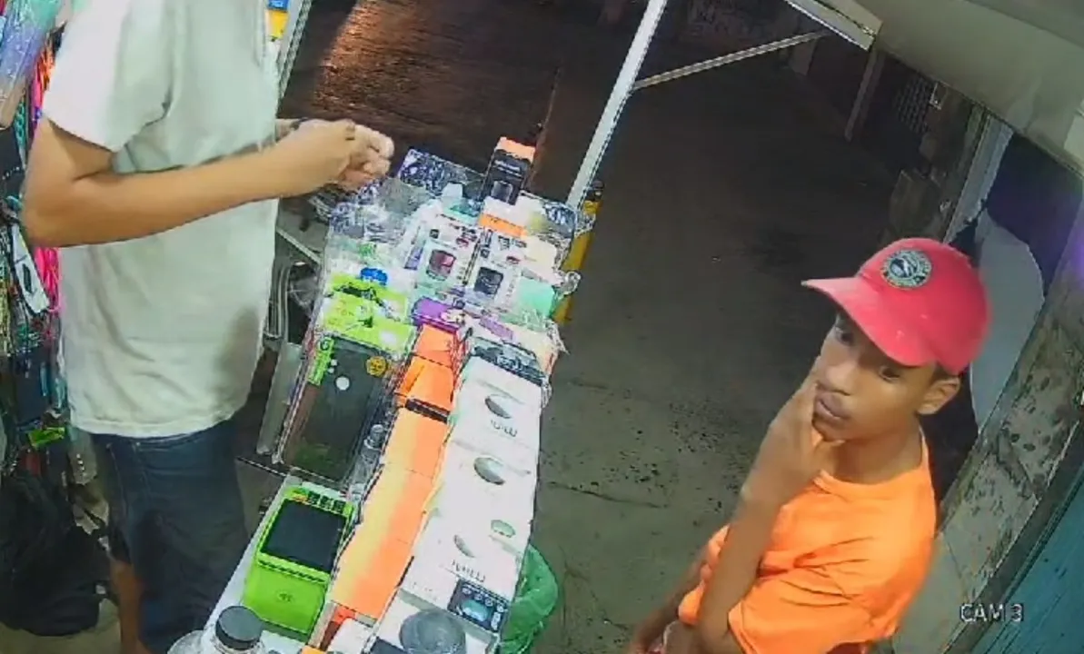 Suspeito pelo crime aparece com uma camisa laranja e boné vermelho conversando com o vendedor