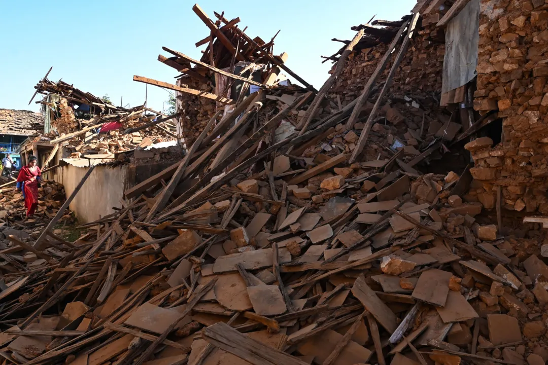 People walk through ruins of houses in the aftermath of an earthquake at Jajarkot district on November 4, 2023. At least 132 people were killed in an overnight earthquake of 5.6-magnitude that struck a remote pocket of Nepal, officials said on November 4, as security forces rushed to assist with rescue efforts. (Photo by Prakash MATHEMA / AFP)