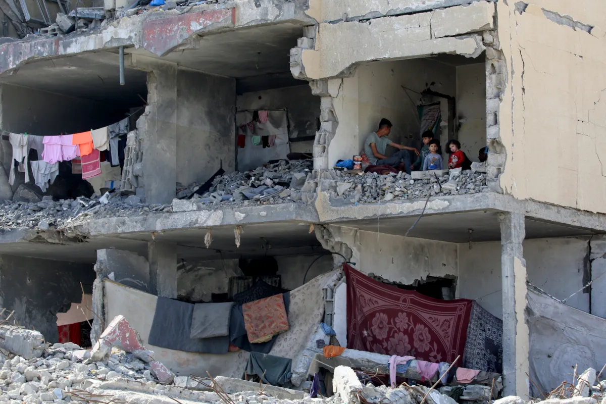 Um homem palestiniano e os seus filhos sentam-se numa sala destruída após o ataque aéreo israelita a um edifício residencial em Rafah, no sul da Faixa de Gaza, a 22 de maio de 2024