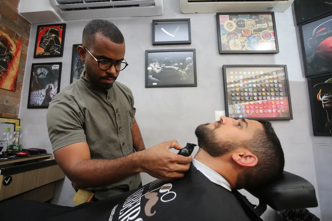 Barbeiro Vitor Formiga fazendo a barba do cliente Caio Damaceno