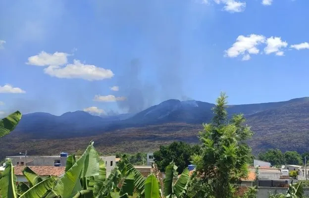 Vegetação seca favorece chamas, que levam fumaça sobre as moradias da cidade; fogo começou 1º de janeiro