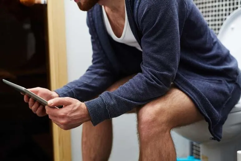 Homem usando tablet enquanto está sentado no vaso sanitário