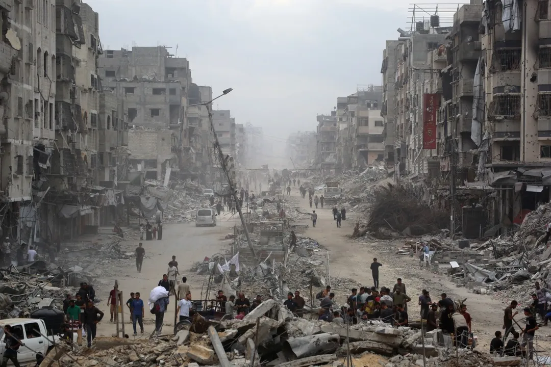 Palestinians make their way past destroyed buildings in Gaza City on October 12, 2025. Hundreds of thousands of Palestinians returned to a devastated Gaza City, after an Israel-Hamas ceasefire came into effect, and as both sides discuss implementing US President Donald Trump's 20-point plan to end the war, which calls for Hamas' disarmament and for the group not to be involved in running post-war Gaza. (Photo by Bashar TALEB / AFP)
