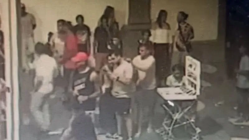 Nas imagens, é possível ver o momento em que um dos suspeitos se aproxima da roda onde algumas pessoas conversavam e arranca a corrente