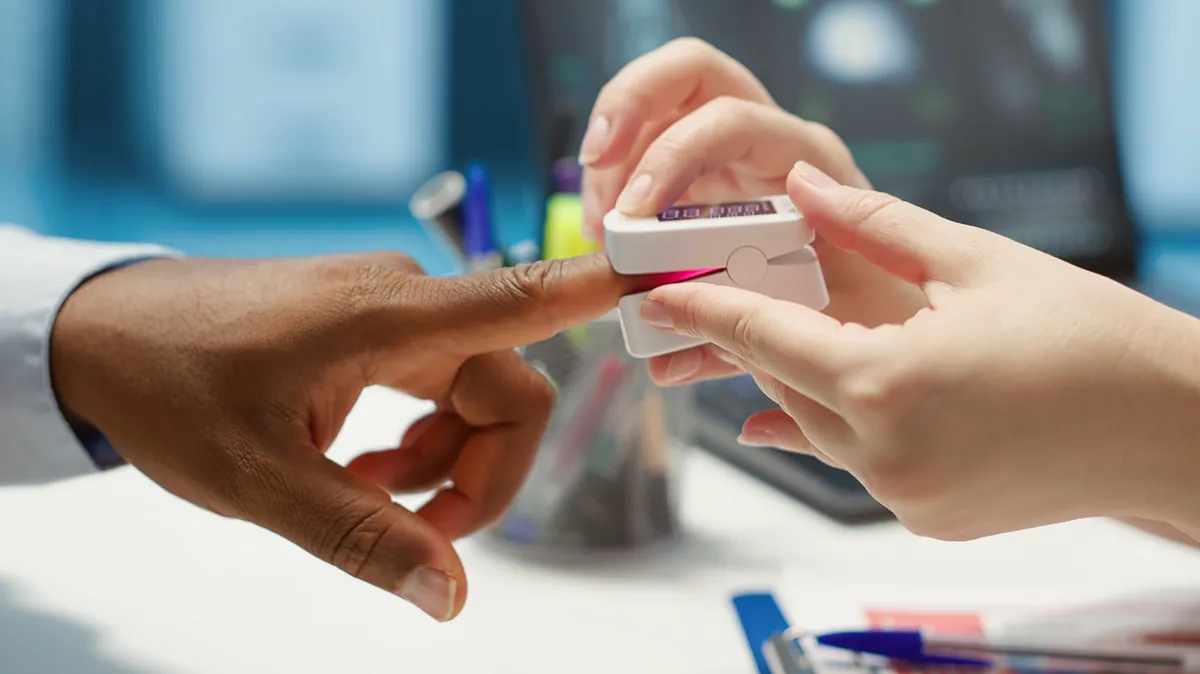 Physician measuring the oxygen saturation and pulse rate using an oximeter during check up visit, consulting her patient with modern medical equipment. Vital signs measurement. Camera A.