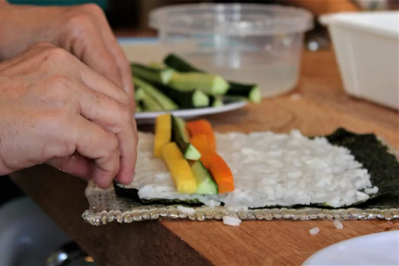 Pegue a alga nori e preencha com arroz; coloque a cenoura, o pepino e a manga 