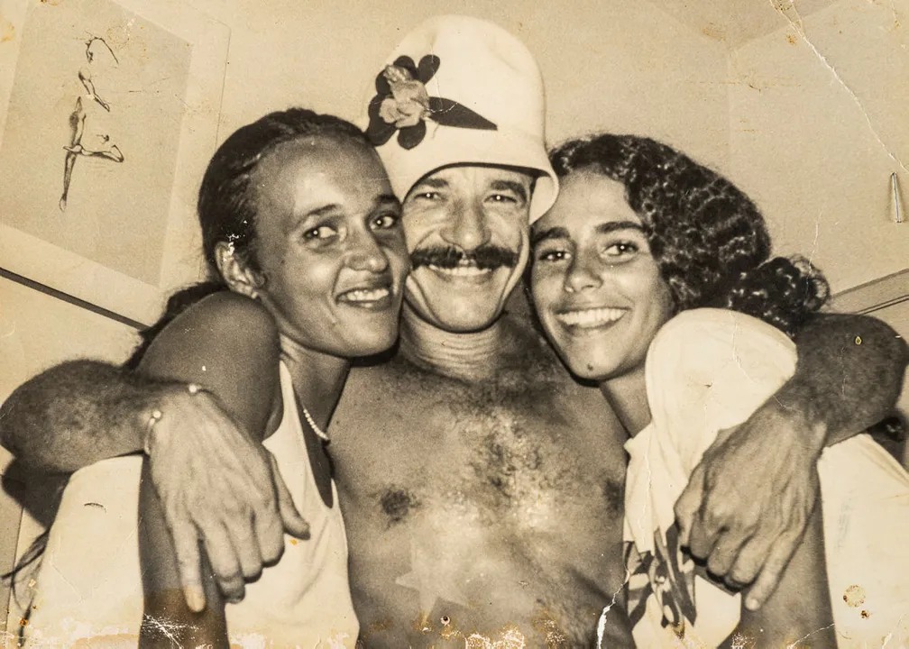 Amantes da noite de Salvador nos anos 1970, 80, e início dos 90, seguramente, frequentaram o Berro d’Água, um bar e restaurante que ficava na famosa esquina da rua Barão de Sergy, no Porto da Barra. Por lá, passaram personalidades nacionais e internacionais proeminentes daquelas décadas.
<br>
<br>
O local foi inaugurado em 20 de maio de 1975, auge da contracultura, e também dos anos de chumbo da ditadura militar implementada no país desde 1964. 
<br>
<br>
Foram 17 anos funcionando com um dos mais importantes pontos de encontro de intelectuais, escritores, jornalistas, publicitários e artistas. Em 2019, houve uma tentativa de tentar trazer o bar de volta, mas a pandemia frustrou esse plano. 
<br>
<br>
As histórias do ponto de encontro viraram até livro. Um de seus fundadores, o itabunense Charles Mocó decidiu colocar suas incontáveis memórias no papel e lançou o livro 'Berro d’Água – Festa, Arte e Boemia na Cidade da Bahia', em 2021.
<br>
<br>
Na foto, o fundador Charles Mocó, abraçado a duas frequentadoras do bar.