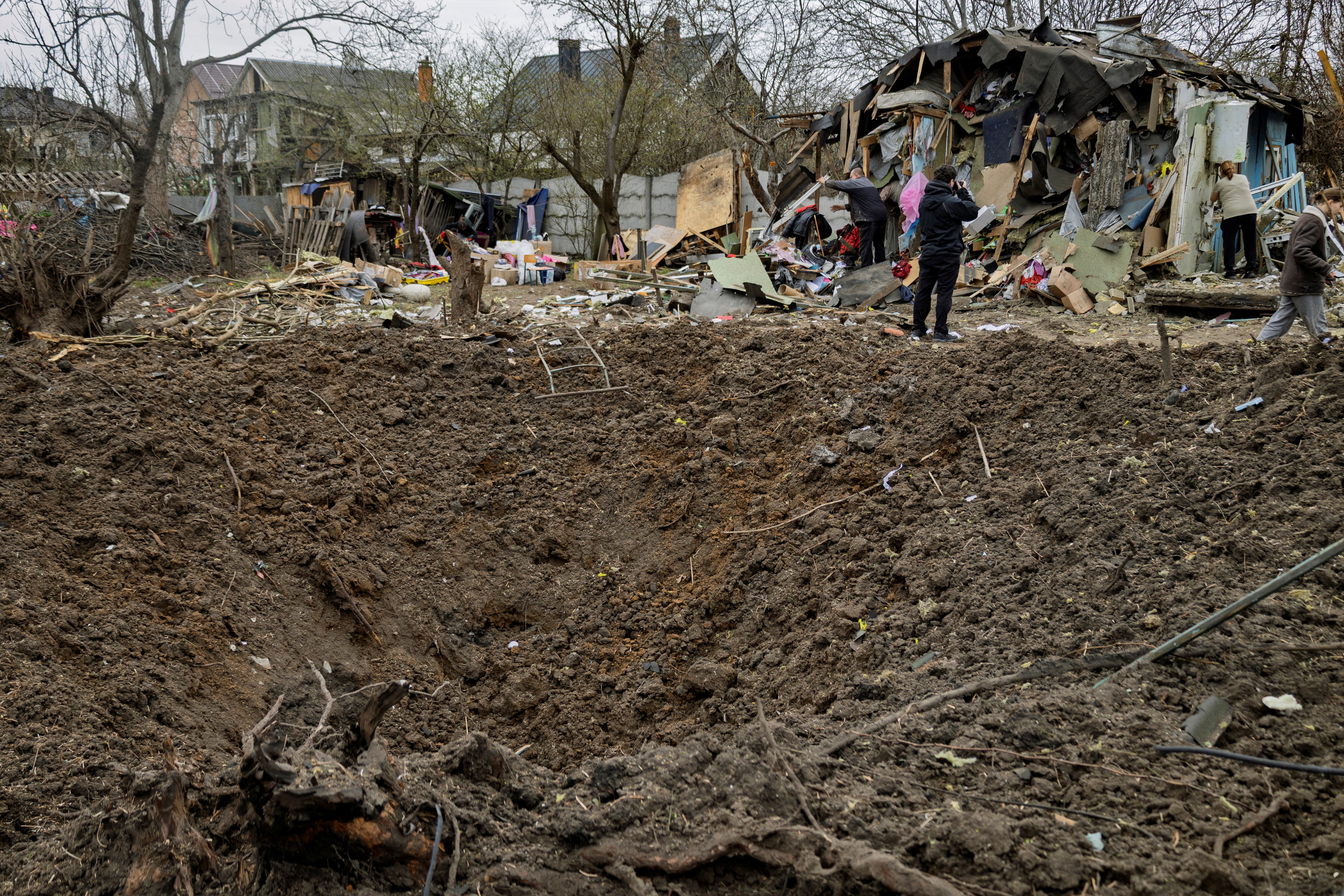 Moradores locais removem os destroços ao lado de uma cratera no local de um ataque aéreo em Kiev, em 16 de abril de 2026, em meio à invasão russa da Ucrânia.