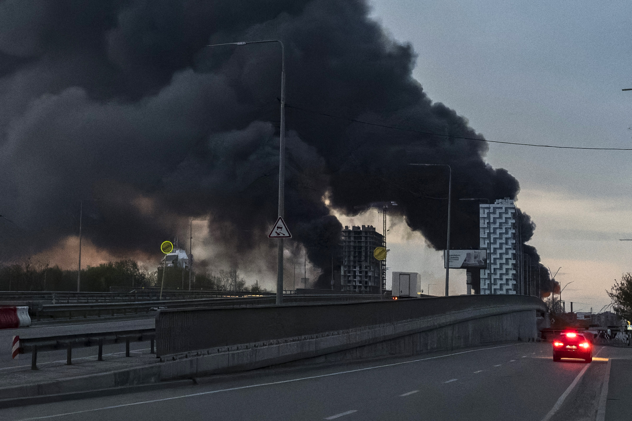 Um carro trafega pela rua enquanto a fumaça sobe acima dos prédios após um ataque aéreo em Kiev, em 16 de abril de 2026, em meio à invasão russa da Ucrânia.