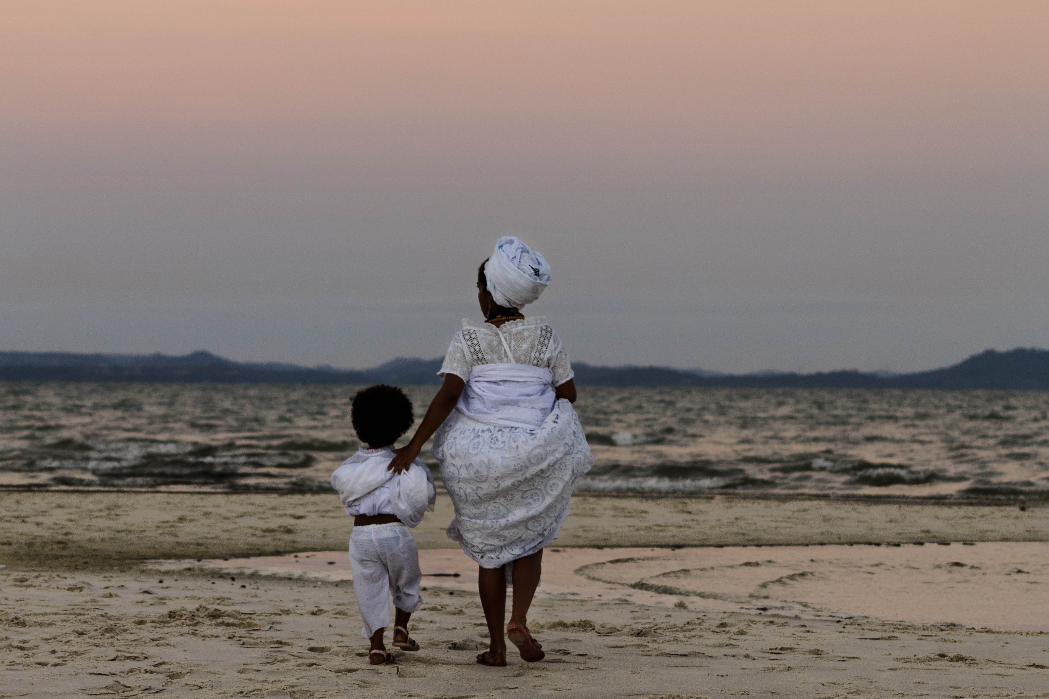 Mãe e filho caminham em direção ao mar, durante a festa do Bembé do Mercado, em Santo Amaro da Purificação