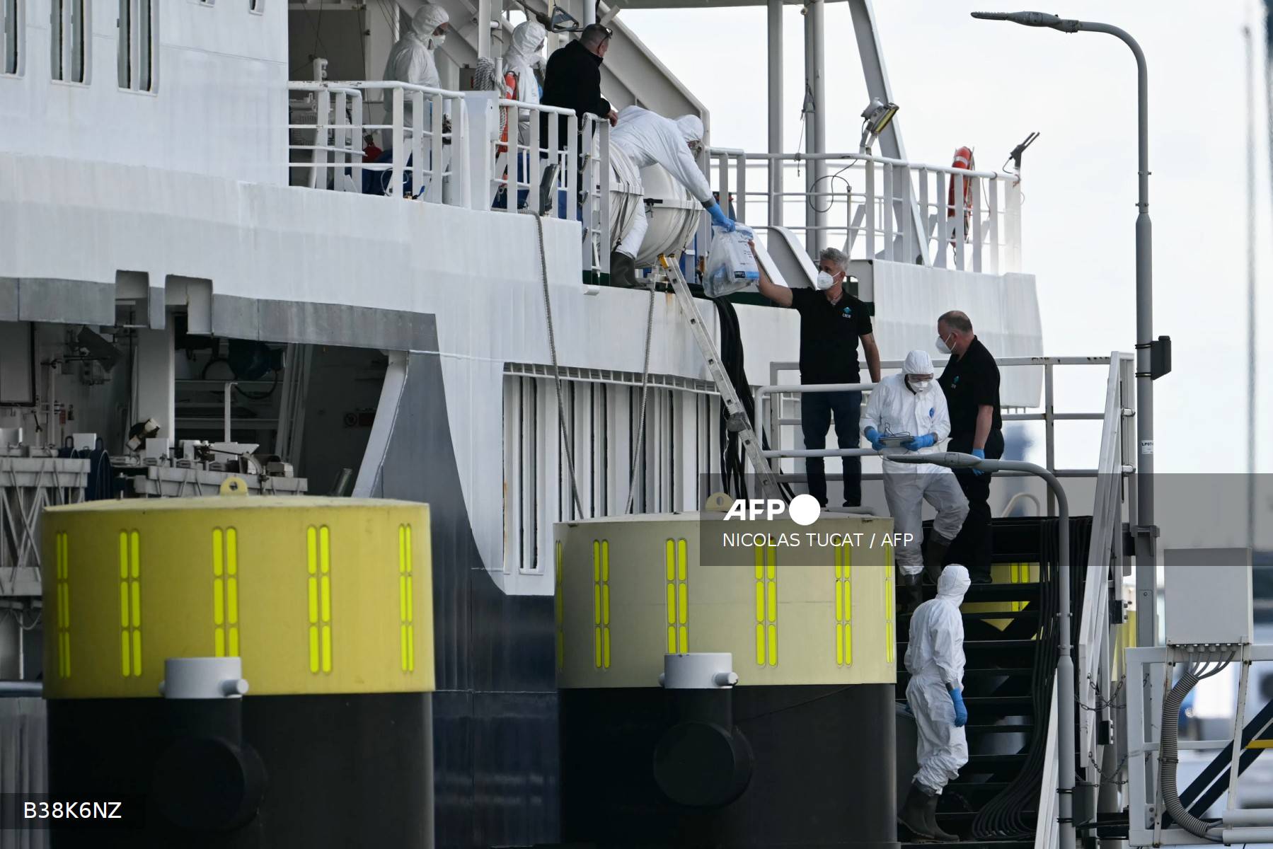 Tripulantes ajudam pessoas vestidas com trajes de proteção contra materiais perigosos, carregando sachês e frascos seláveis, a desembarcar do navio de cruzeiro holandês MV Hondius, atingido pelo hantavírus e atracado no porto de Roterdã em 18 de maio de 2026.