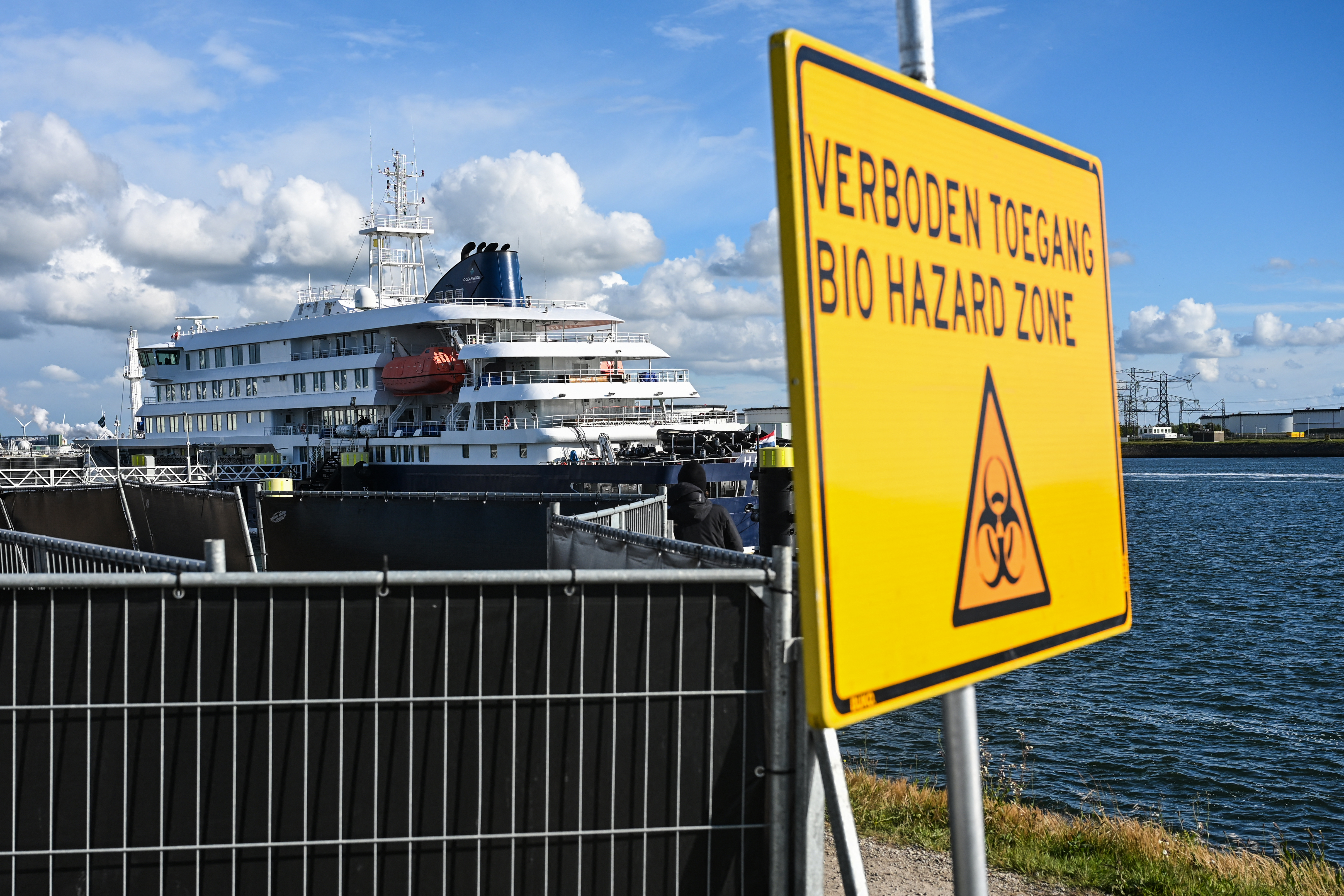 Placa com a inscrição "Zona de risco biológico" e, ao fundo, o navio de cruzeiro holandês MV Hondius.