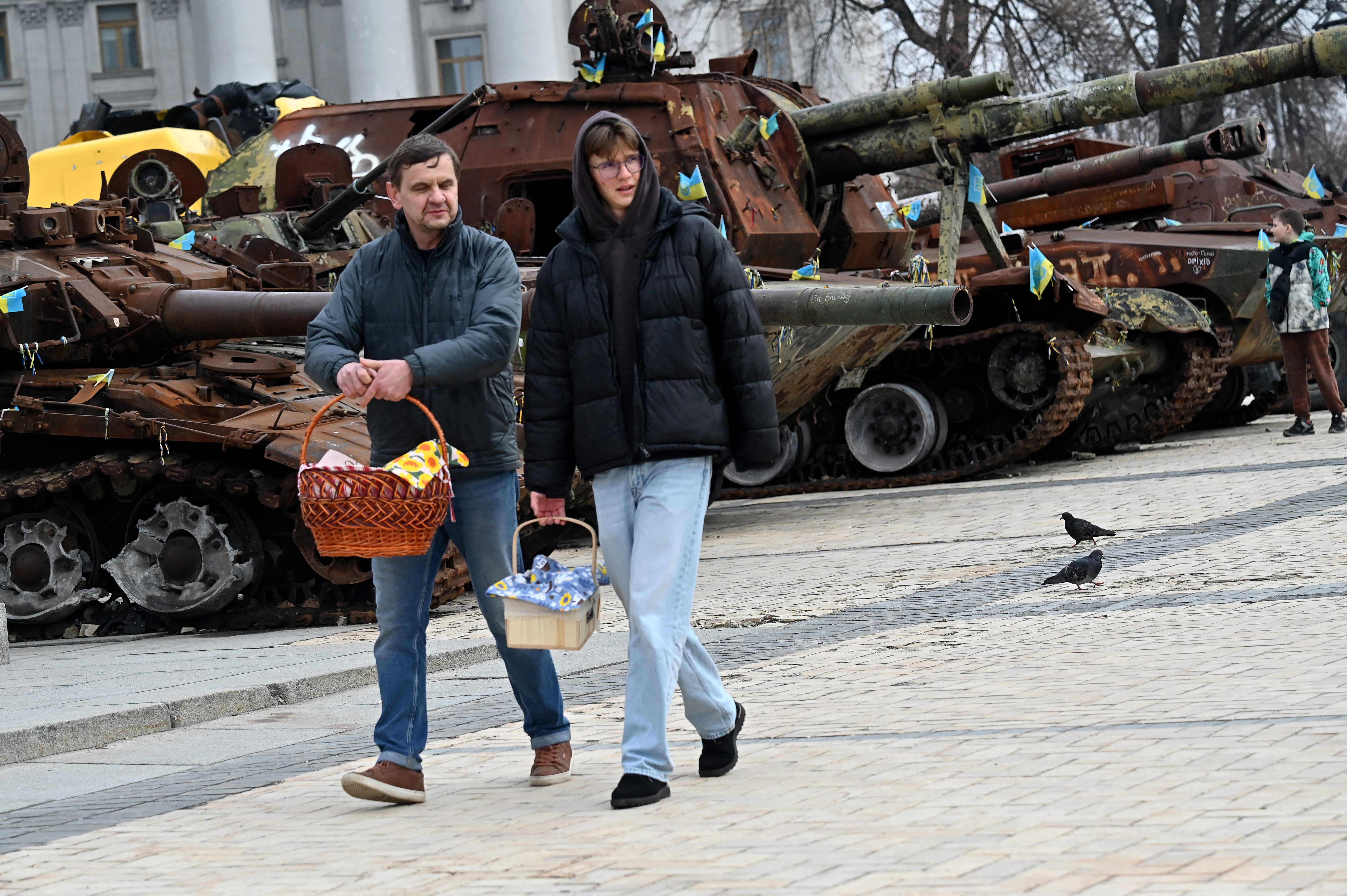 Moradores locais carregam suas cestas repletas de bolos e ovos tradicionais enquanto passam por uma exposição a céu aberto de equipamentos militares russos destruídos durante as celebrações da Páscoa em Kiev