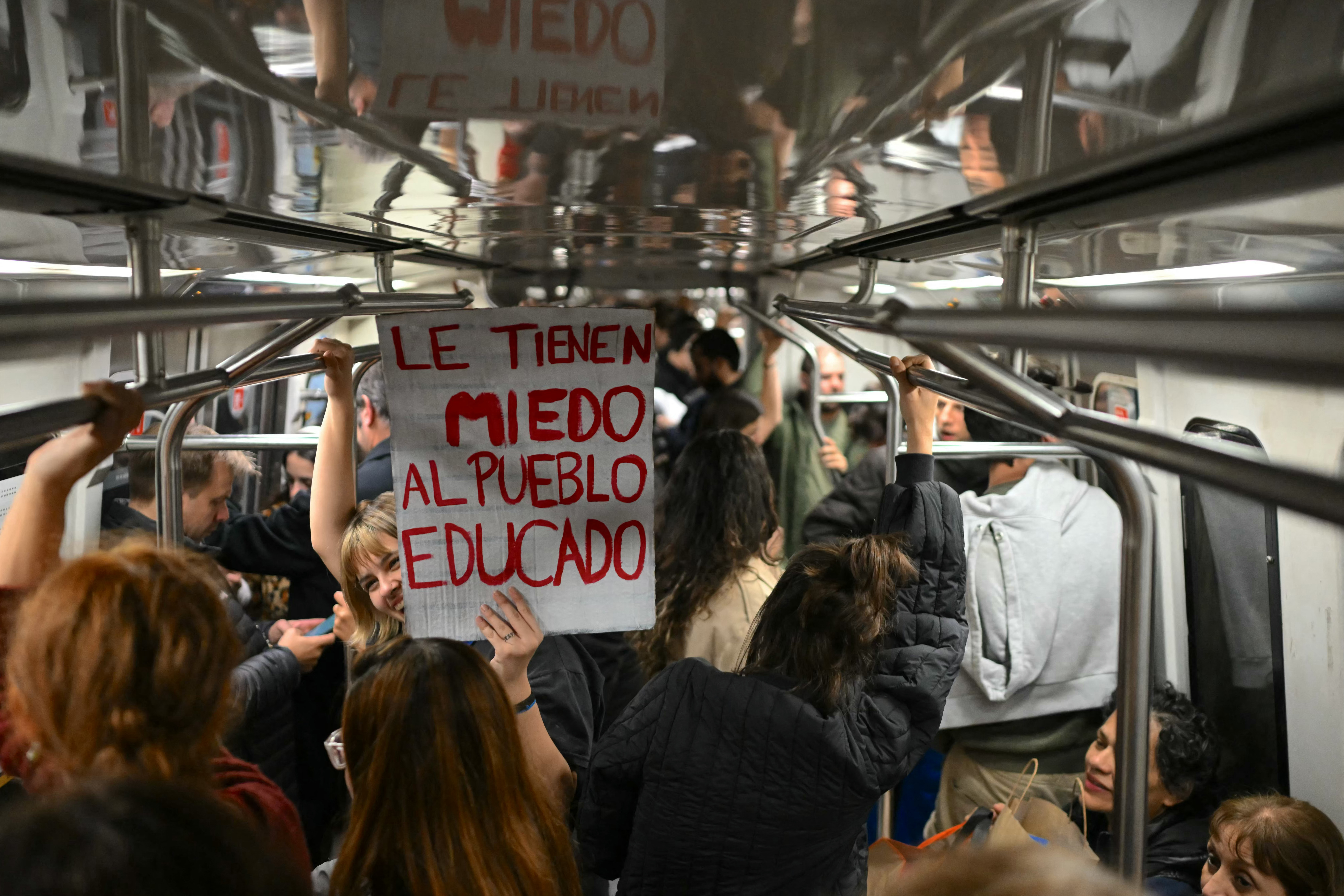 Uma mulher segura uma faixa com os dizeres "Eles têm medo das pessoas instruídas" em um vagão do metrô