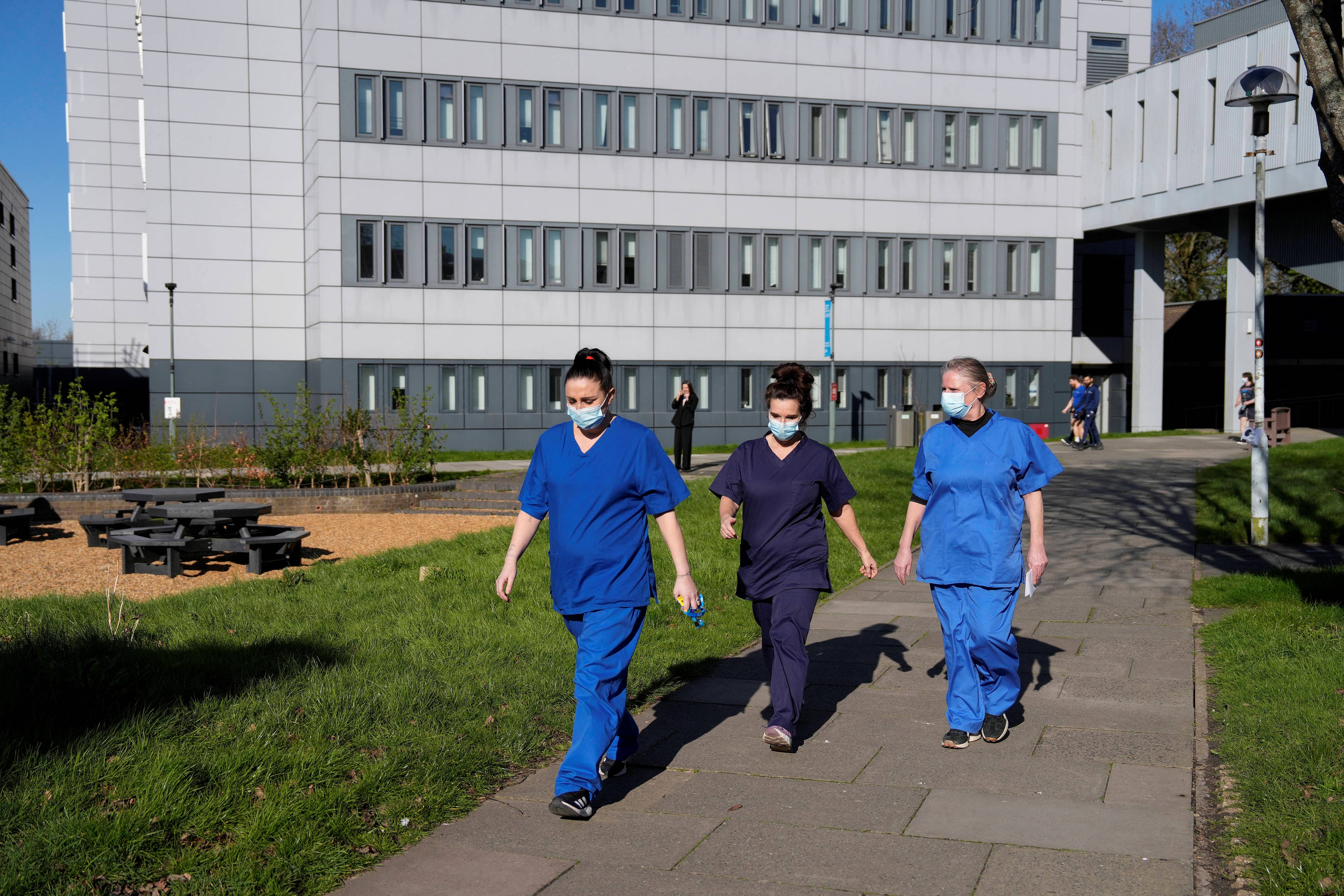 Pessoas vestindo uniformes médicos e máscaras faciais caminham pelo campus da Universidade de Kent em Canterbury