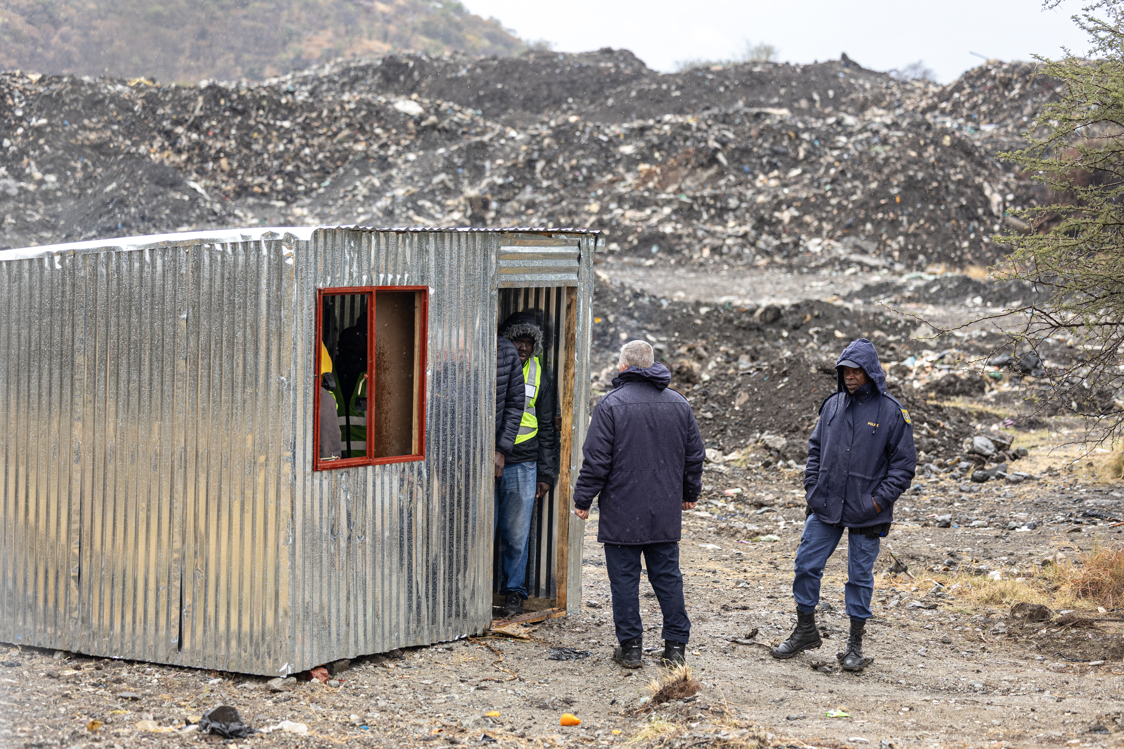 Policiais do Serviço de Polícia da África do Sul (SAPS) conversam com agentes de segurança perto de um poço de mina em Nkaneng, próximo a Marikana, em 11 de agosto de 2026, onde 14 mineiros ilegais foram encontrados mortos enquanto operações de resgate estão em andamento.