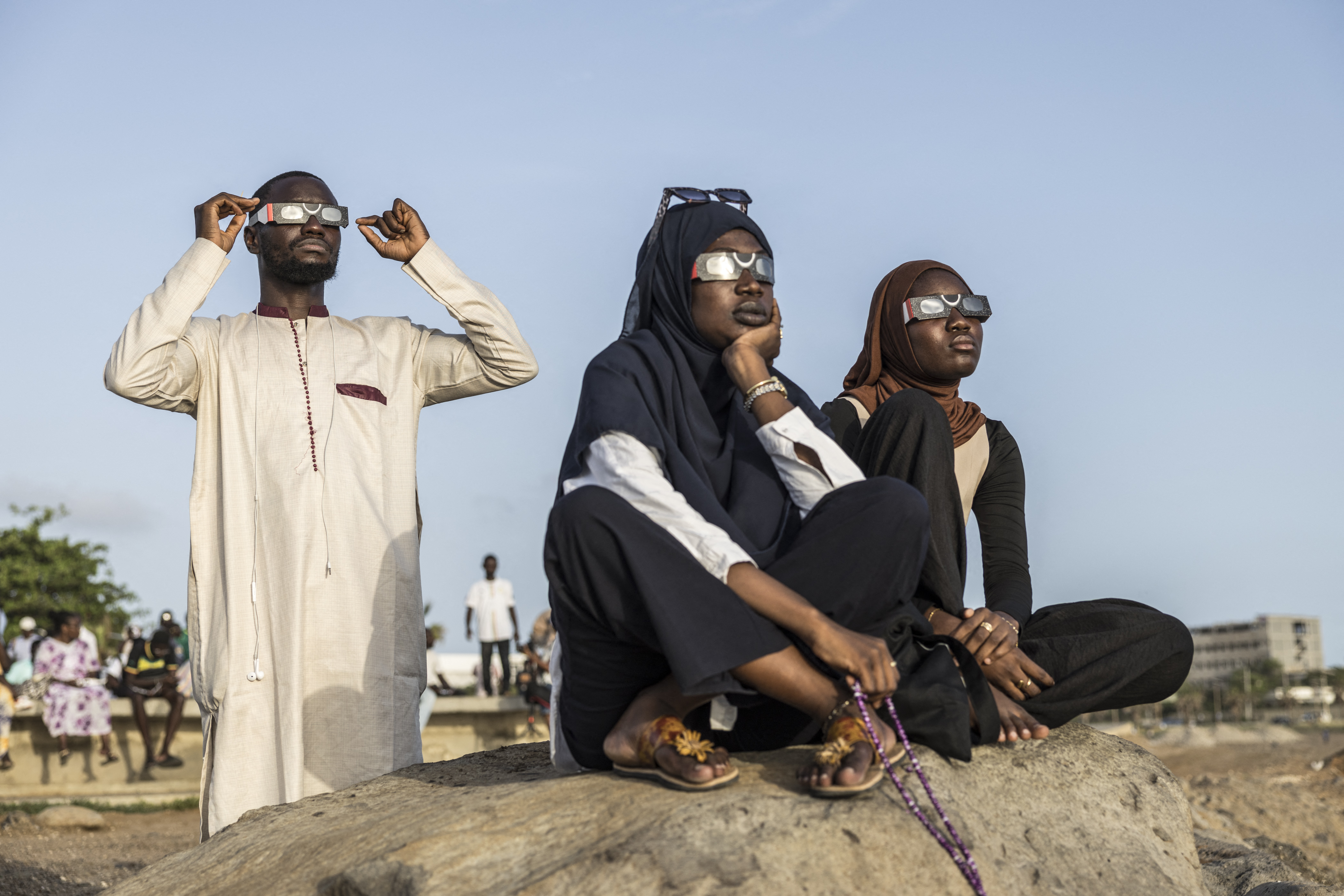 Pessoas observam, com óculos de proteção solar, a Lua passar diante do Sol durante um eclipse solar parcial em Dakar, em 12 de agosto de 2026.