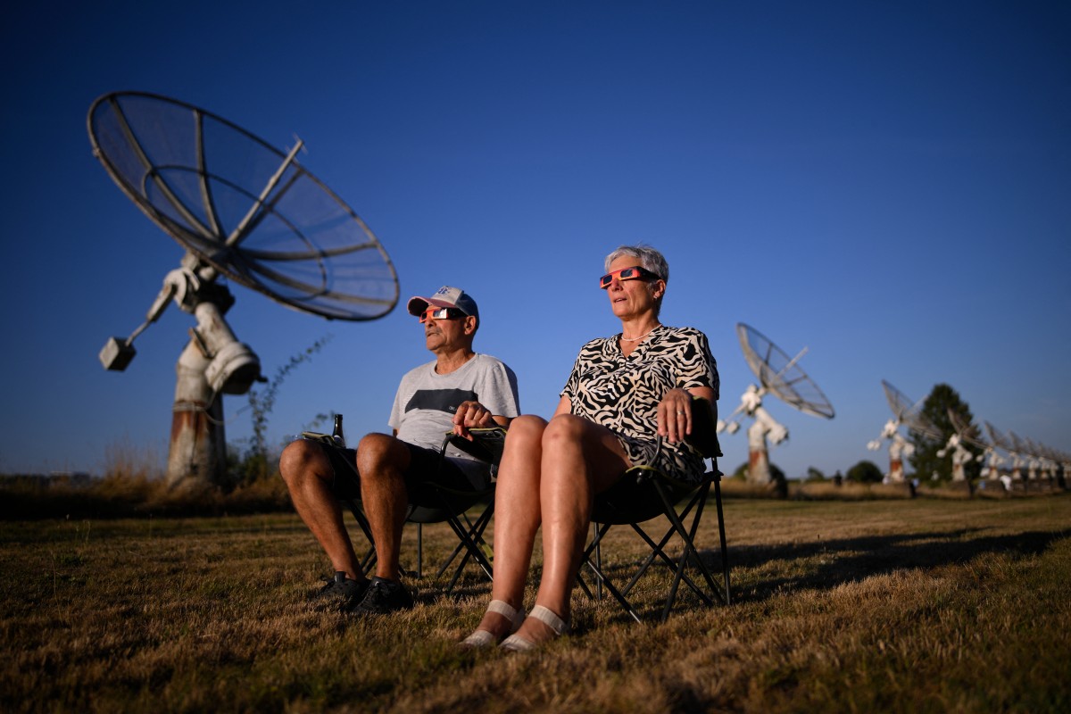 Pessoas observam o fenômeno com óculos de proteção enquanto a Lua cruza o disco solar durante um eclipse solar parcial no Observatório Real da Bélgica, em Marche-en-Famenne, no sul do país.