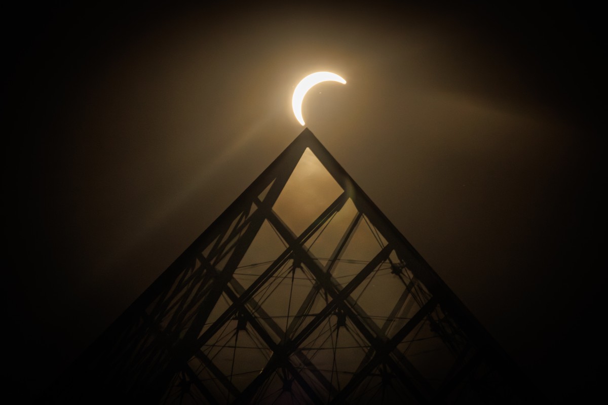 A Lua passa sobre o horizonte do Sol atrás da Pirâmide do Louvre, projetada pelo arquiteto sino-americano Ieoh Ming Pei, durante um eclipse solar parcial em Paris, em 12 de agosto de 2026.