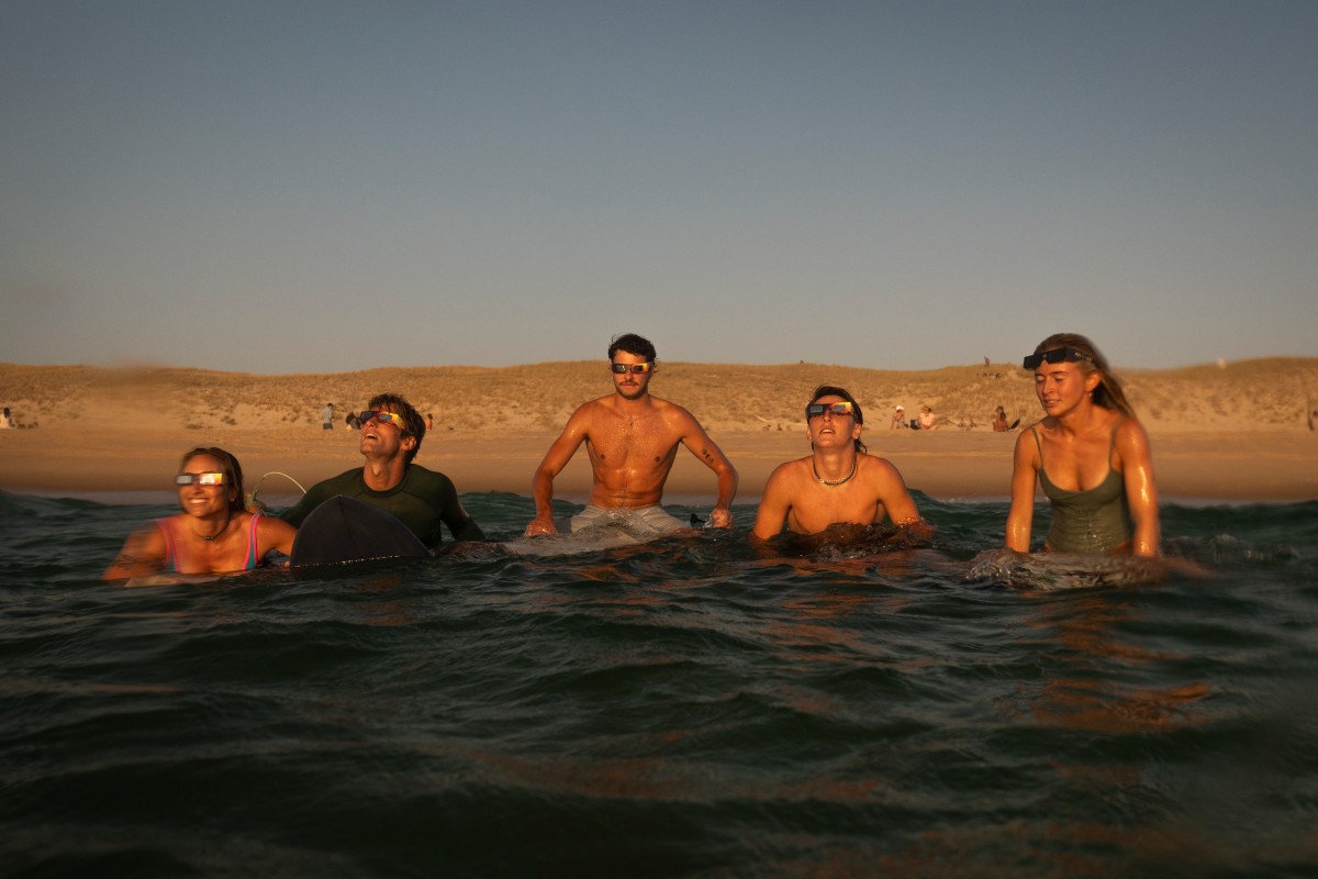 Surfistas observam um eclipse solar parcial dentro da água em Lège-Cap-Ferret, em 12 de agosto de 2026. Milhões de pessoas voltam o olhar para o céu em 12 de agosto de 2026 para testemunhar um dos maiores espetáculos da natureza — um raro eclipse solar total.