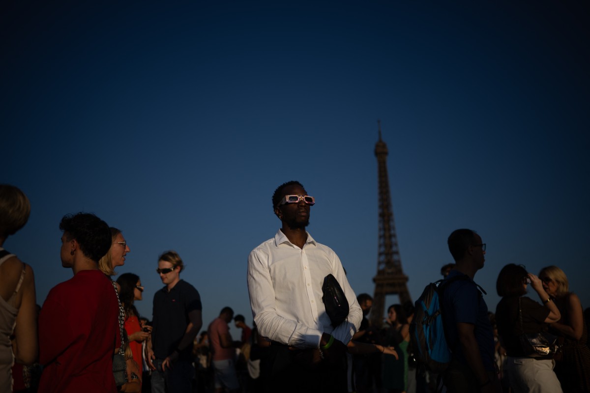 Pessoas usando óculos para observação de eclipse solar observam um eclipse solar parcial da Praça do Trocadéro, com a Torre Eiffel ao fundo, em Paris, em 12 de agosto de 2026.