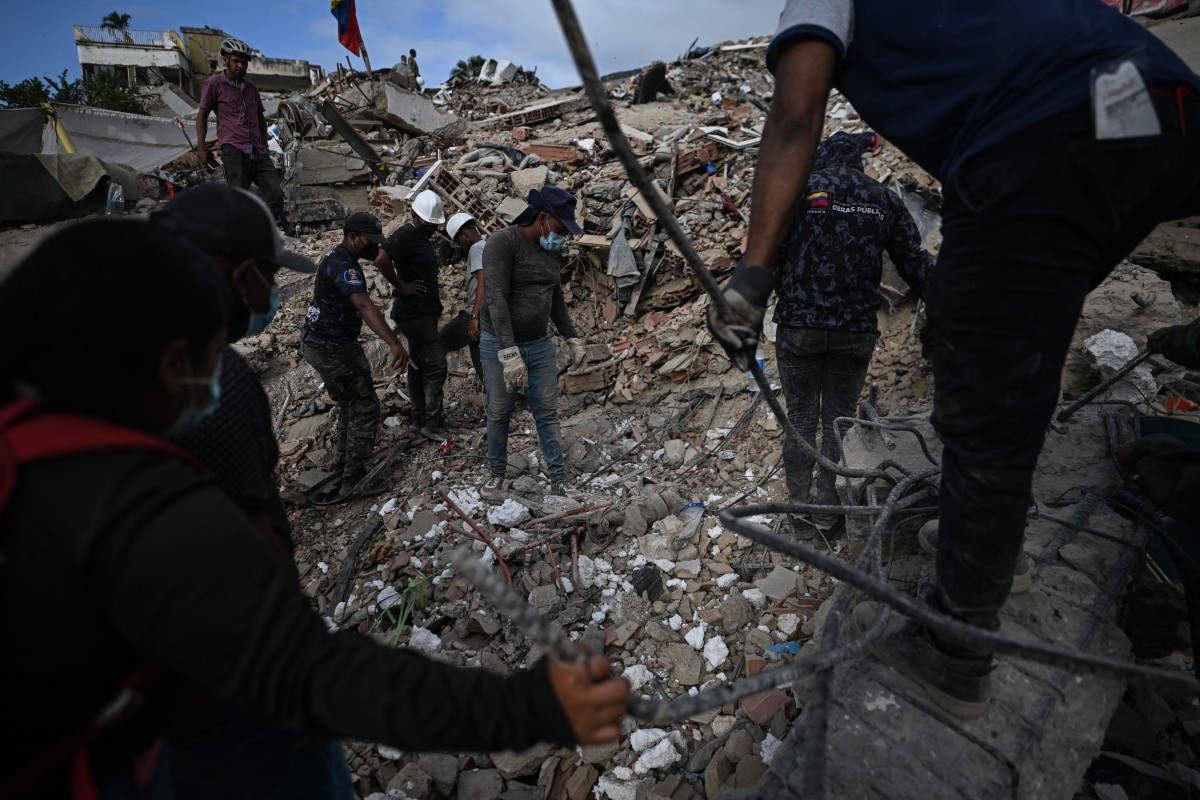Pessoas buscam corpos em meio aos escombros de um prédio em Caraballeda, na Venezuela, em 22 de julho de 2026, quase um mês após os terremotos de 24 de junho