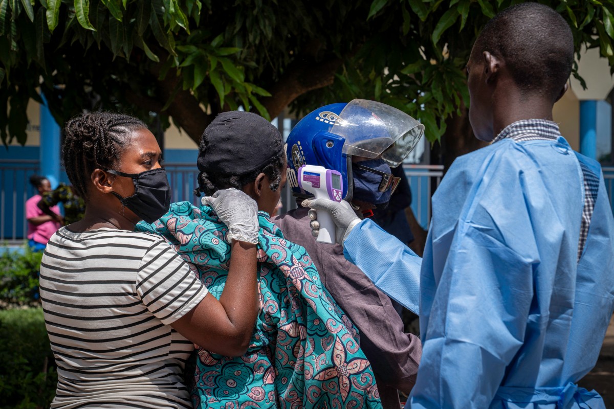 Um profissional de saúde (à direita) mede a temperatura de uma paciente (segunda à esquerda) com suspeita de Ebola enquanto ela é transportada de mototáxi para o Hospital de Rwampara, em Ituri, no leste da República Democrática do Congo, em 26 de maio de 2026.