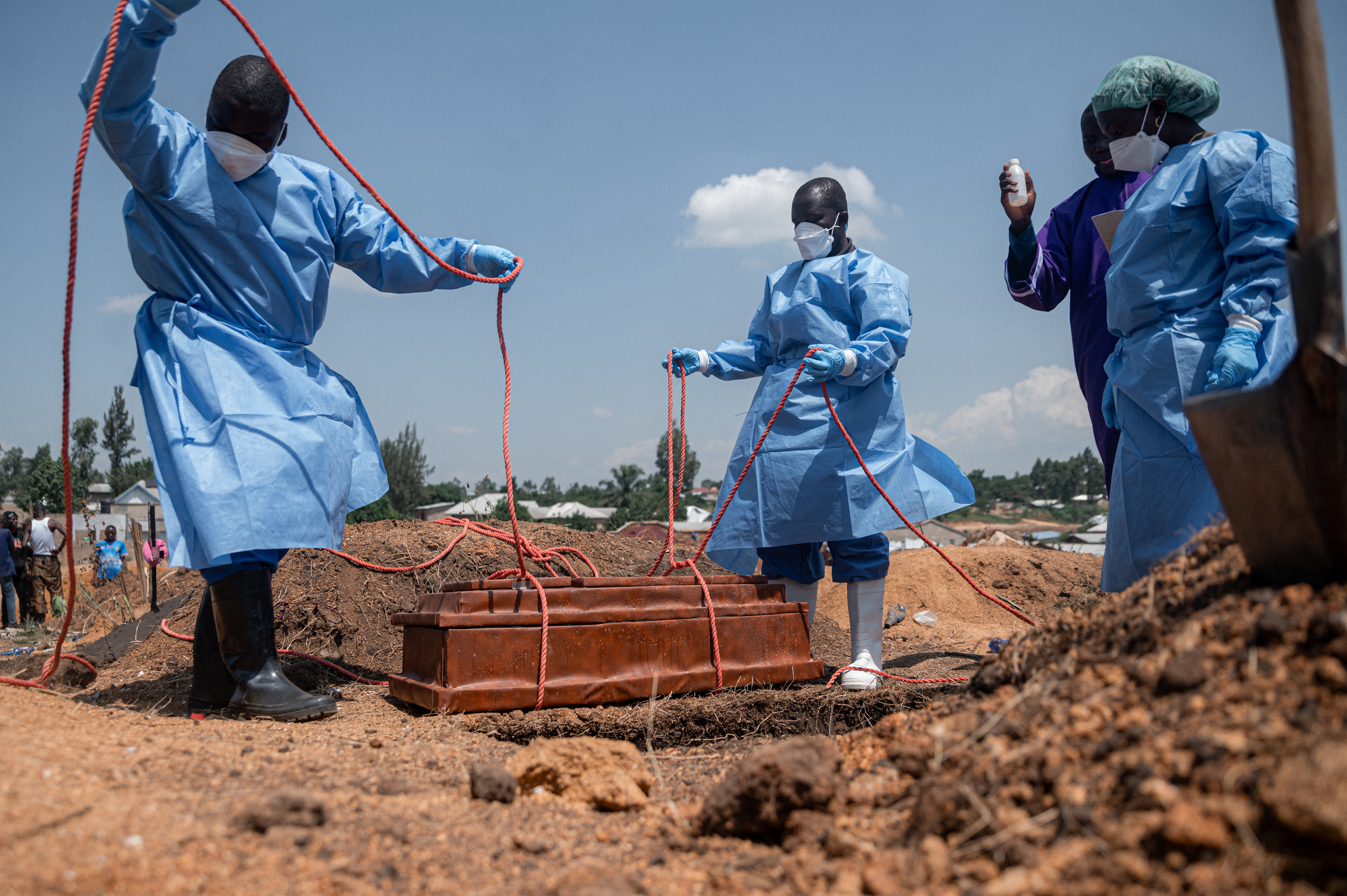 Equipes da Federação Internacional das Sociedades da Cruz Vermelha e do Crescente Vermelho preparam o sepultamento, no cemitério de Mbiyo, do corpo de um quarto órfão que morreu em decorrência da doença pelo vírus Ebola em um orfanato em Bunia, na província de Ituri, em 19 de junho de 2026.