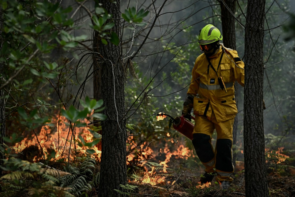 Um bombeiro avalia a situação em meio à fumaça, segurando um maçarico de gotejamento metálico durante uma operação de queima controlada em uma floresta em Le Porge, ao norte da Bacia de Arcachon, em 30 de julho de 2026, durante os incêndios florestais na região de Gironde, no sudoeste da França.