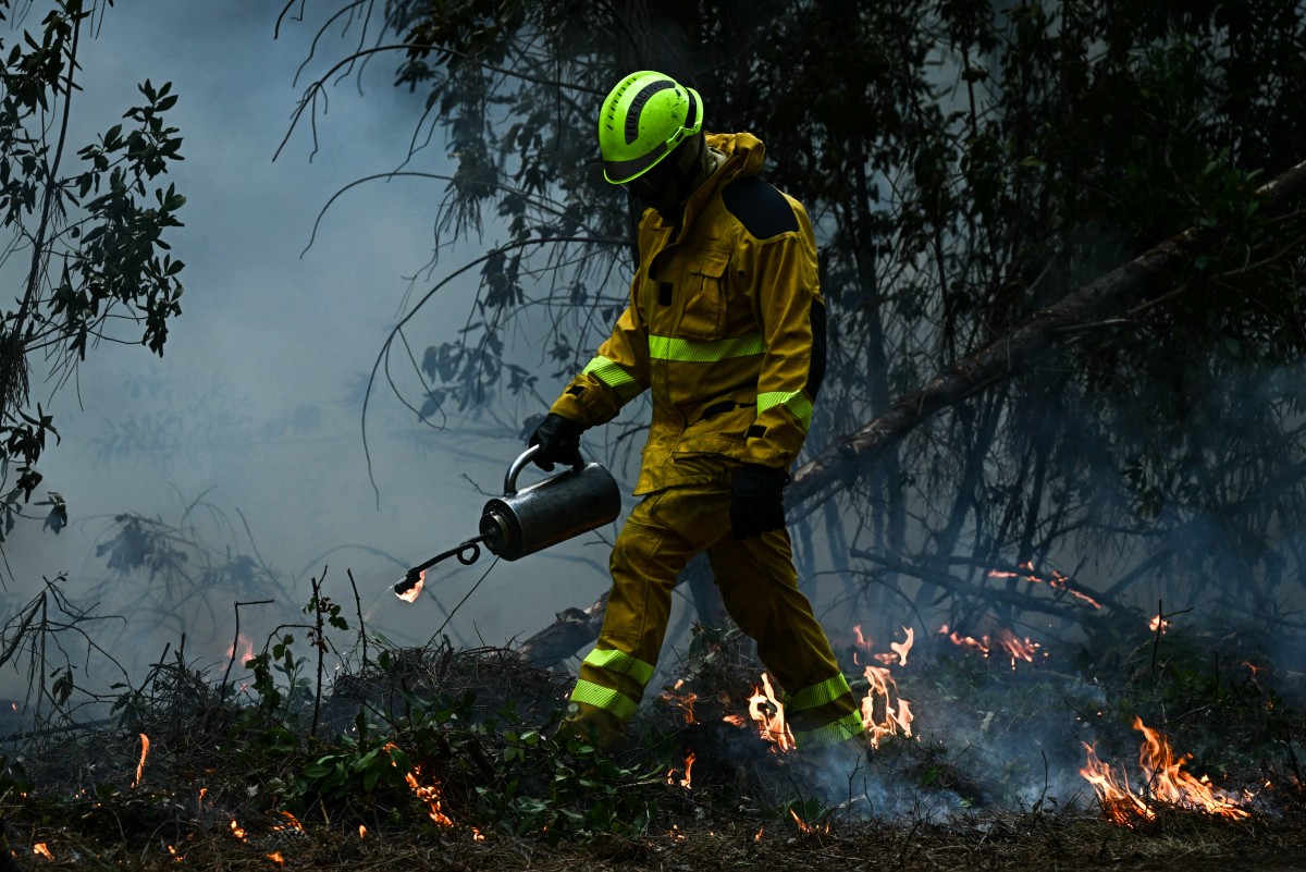Um bombeiro utiliza um maçarico de gotejamento metálico para iniciar queimadas controladas em uma floresta em Le Porge, ao norte da Bacia de Arcachon, em 30 de julho de 2026, durante incêndios florestais na região de Gironde, no sudoeste da França.