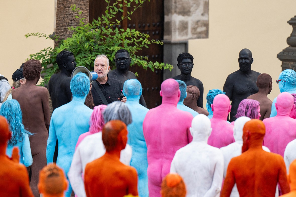 Participantes se preparam para posar nus e com o corpo pintado enquanto o fotógrafo americano Spencer Tunick (acima, à esquerda) fala antes de fazer as fotos para sua intervenção artística coletiva "Grand Spectrum", na praça Santa Ana, no bairro de Vegueta, em Las Palmas de Gran Canaria, em 26 de julho de 2026.