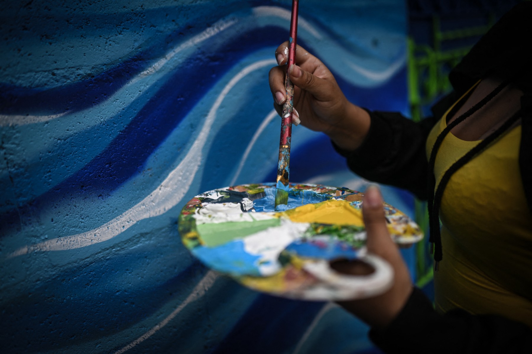 A artista salvadorenha Marcela Alvarenga segura uma paleta de pintura enquanto trabalha no mural "Identidade", na comunidade 10 de Octubre, em San Marcos, El Salvador.