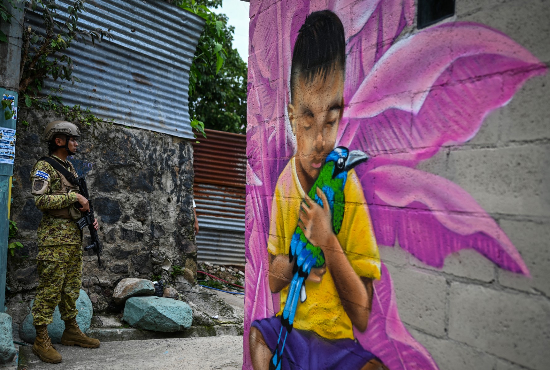 Um soldado salvadorenho faz a guarda na comunidade 10 de Octubre, em San Marcos, El Salvador, enquanto a artista Elizabeth Guardado pinta o mural "Identidade", em 2 de outubro de 2026.