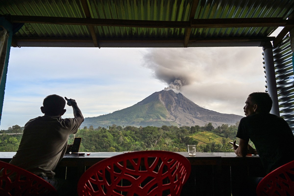Dois homens observam o Monte Sinabung expelir cinzas e fumaça densa, vistos de Karo, na província de Sumatra do Norte, no início de 2 de setembro de 2026.