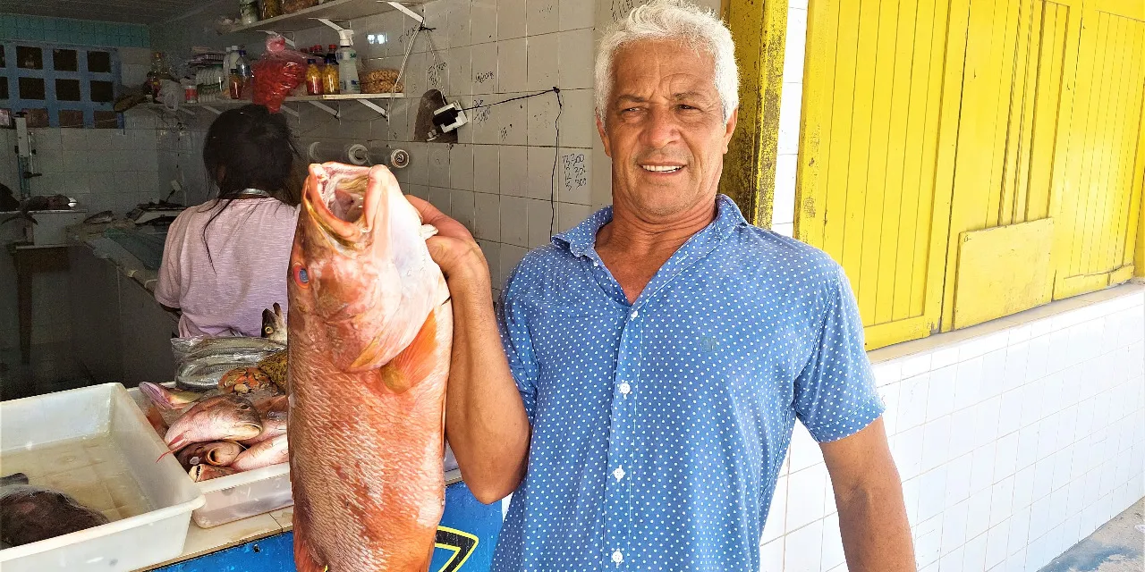 O pescador Paulo César Mota carrega um vermelho de 7kg em frente a sua peixaria na Praia de Guarajuba  