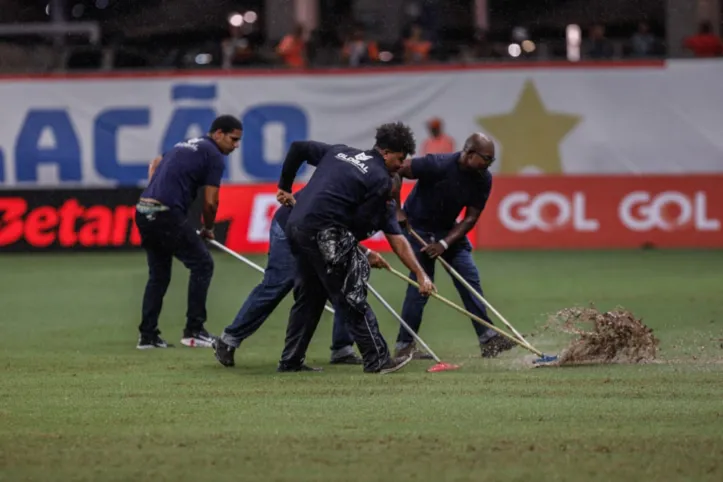 Com ajuda de rodos, funcionários drenam a água do gramado