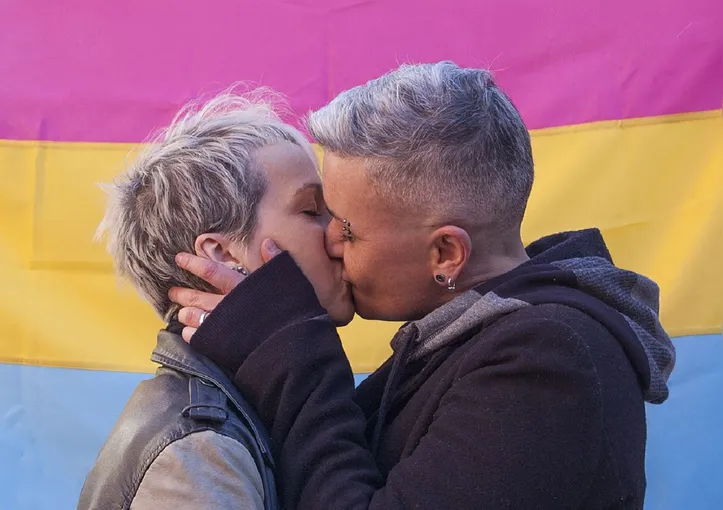 Casal se beijando em frente da bandeira pansexual