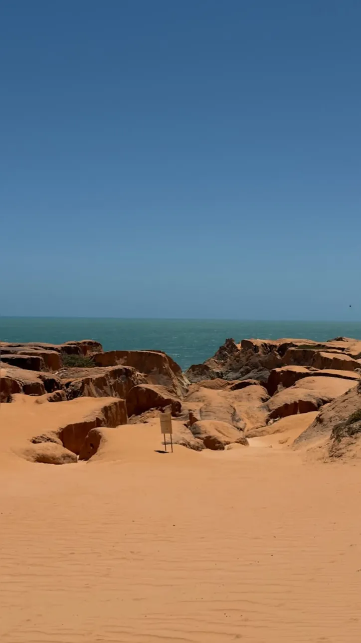Formações rochosas de tons avermelhados desenham o caminho natural em Morro Branco que segue até o mar