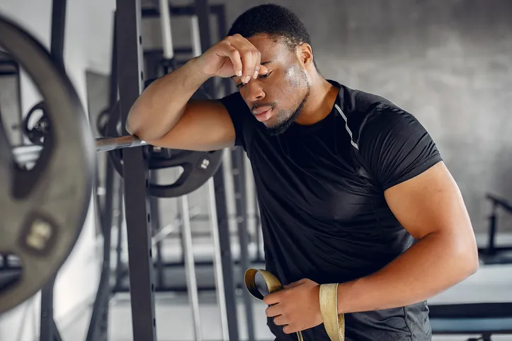 Sports man in the gym. A black man performs exercises. Guy in a black t-shirt